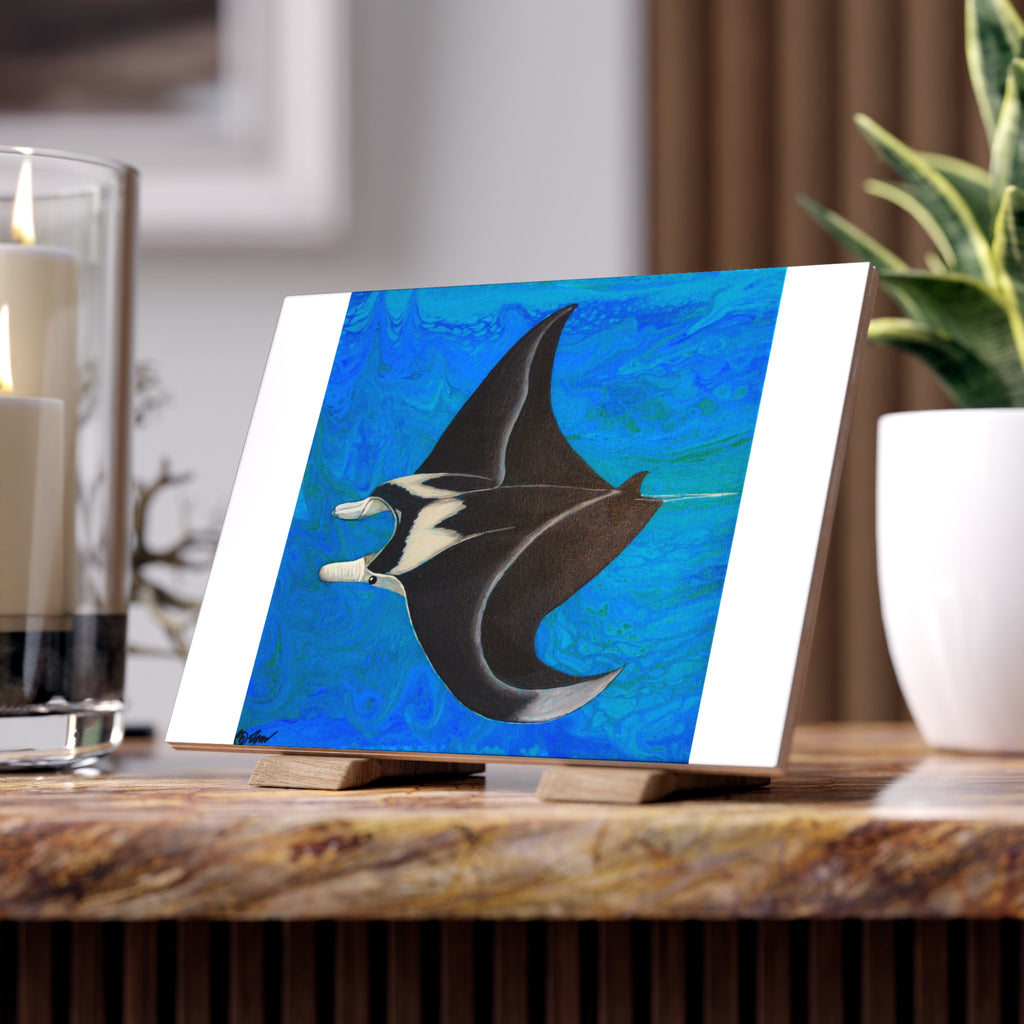 Artistic depiction of a manta ray on a blue background tile, placed on a wooden surface with candles and a plant in the background.