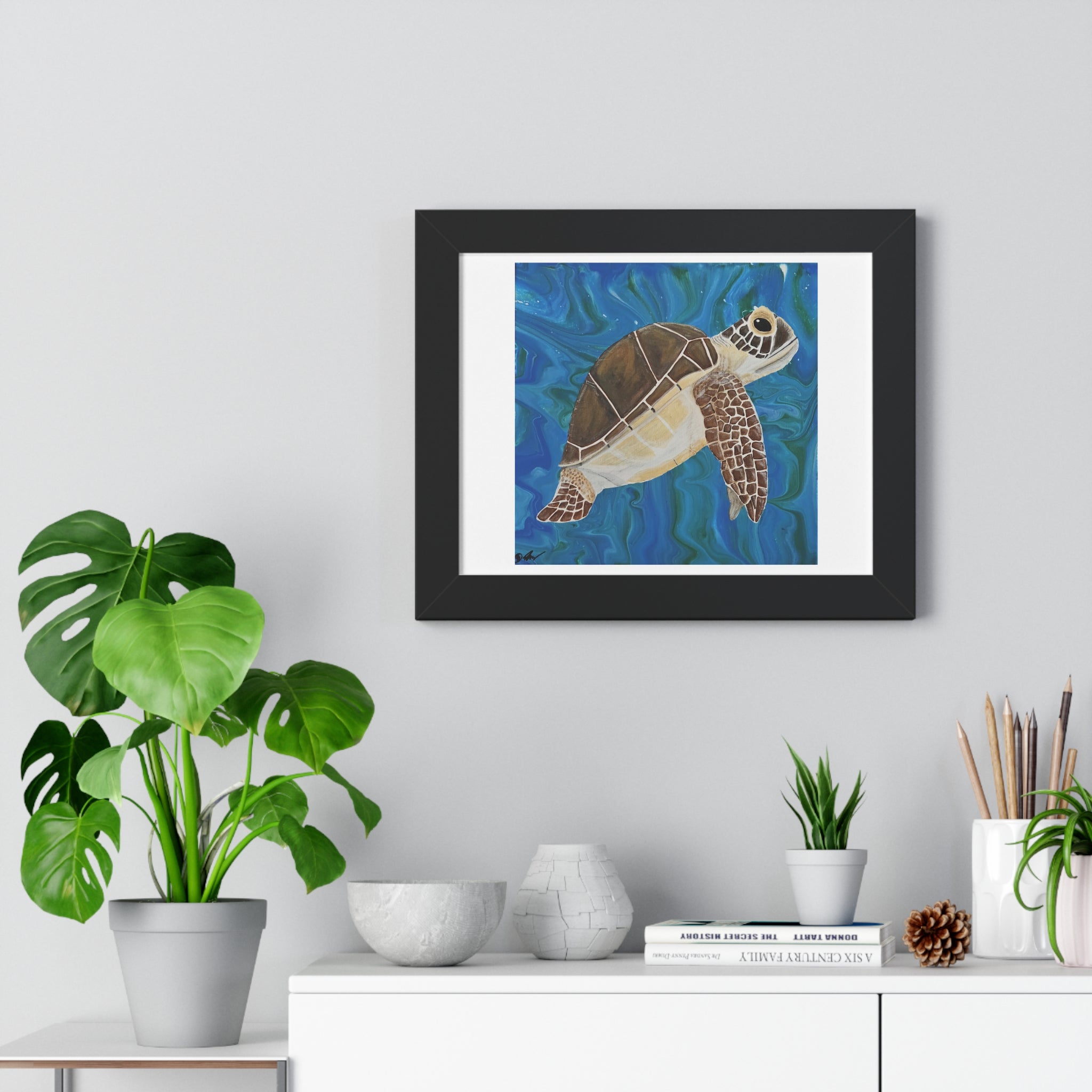 Framed artwork of a turtle on a wall above a white cabinet with decorative items.