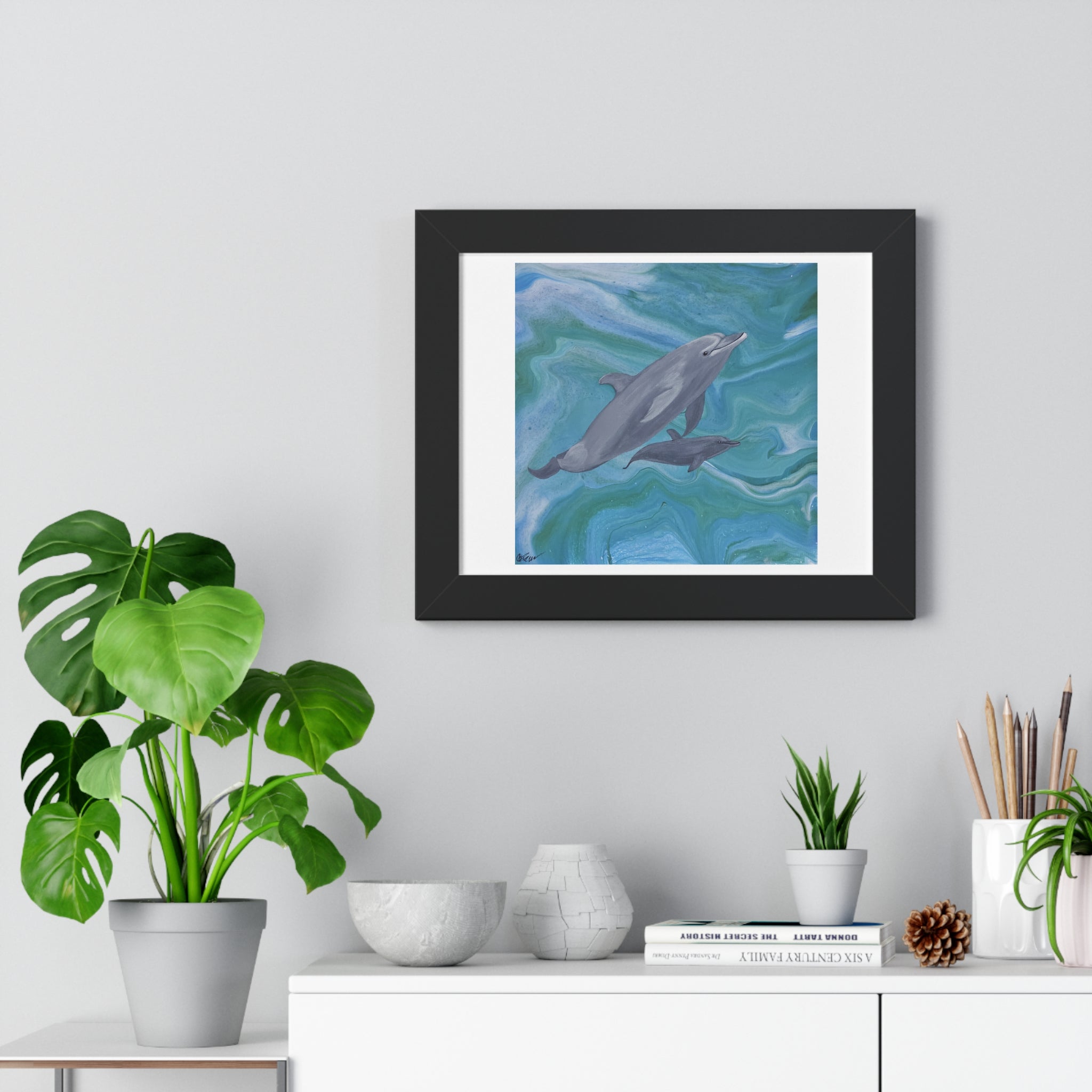 Framed artwork of dolphins on a wall above a white cabinet with decorative items.