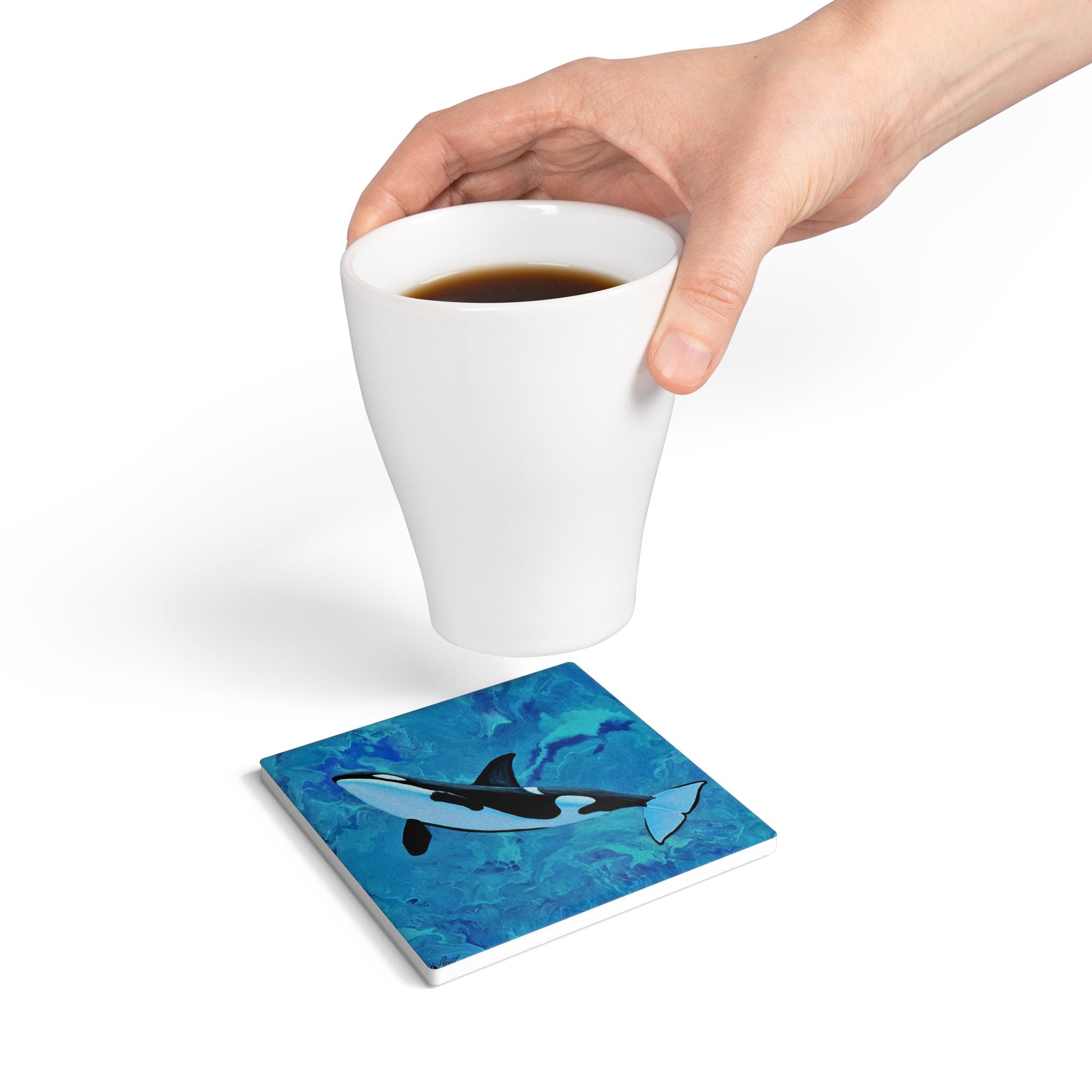 Coaster with whale design on a white surface, hand holding a cup of coffee.