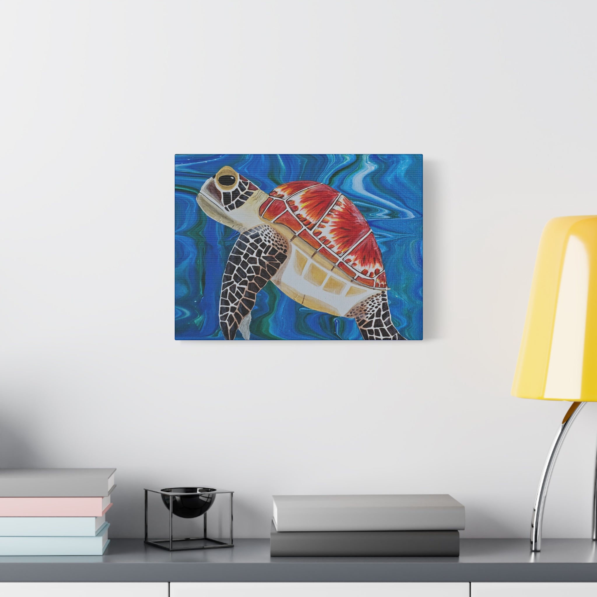 Canvas print of a turtle painting on a wall above a desk with books and a lamp.
