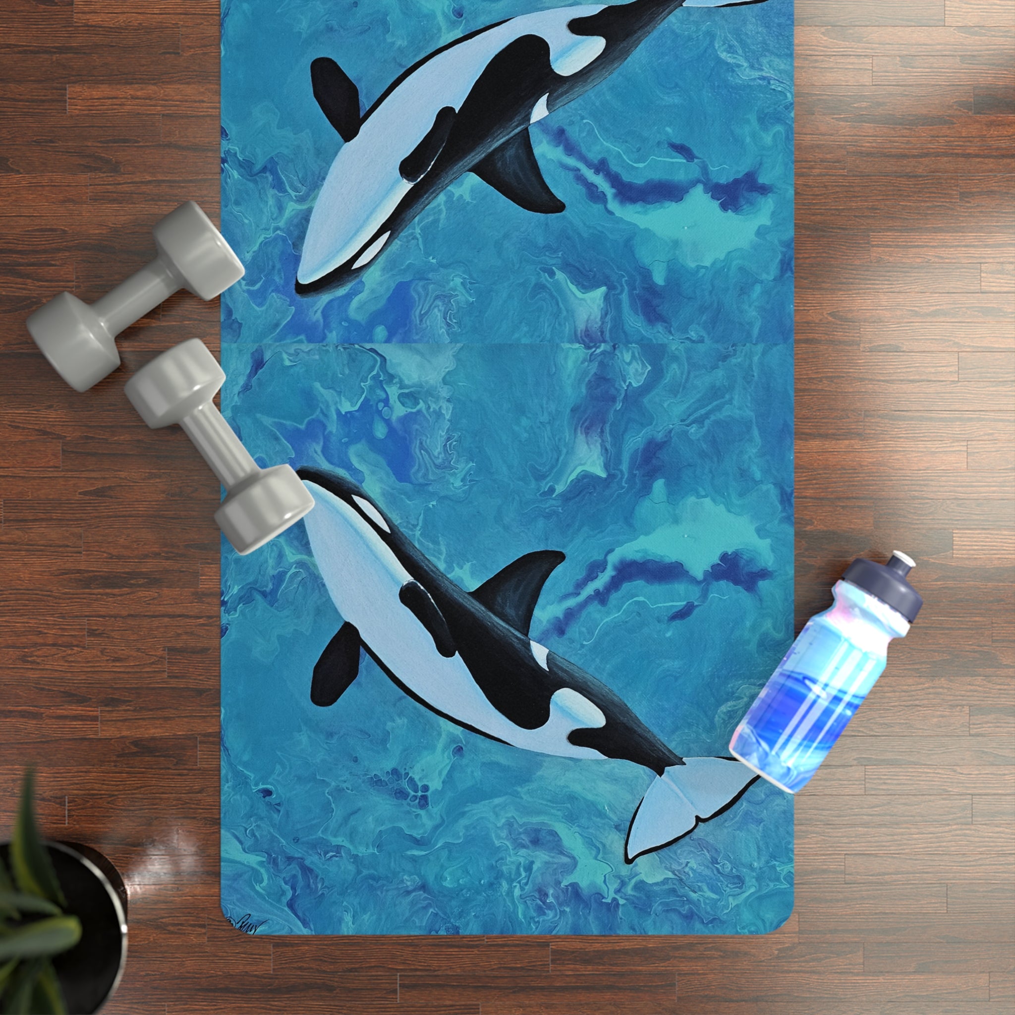 Yoga mat with orca whale design on a wooden floor with dumbbells and a water bottle.