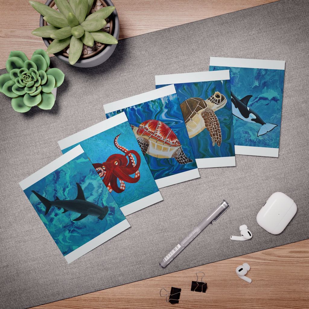 Set of greeting cards with underwater animal designs on a desk with office supplies.