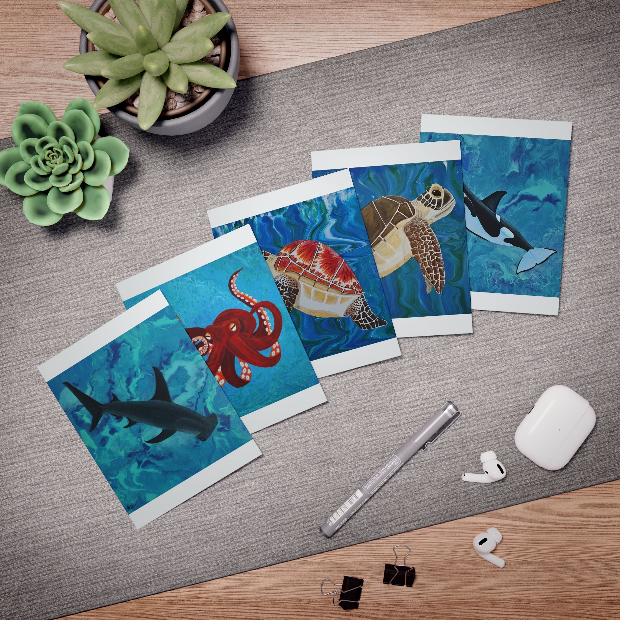 Set of greeting cards with underwater animal designs on a desk with office supplies.