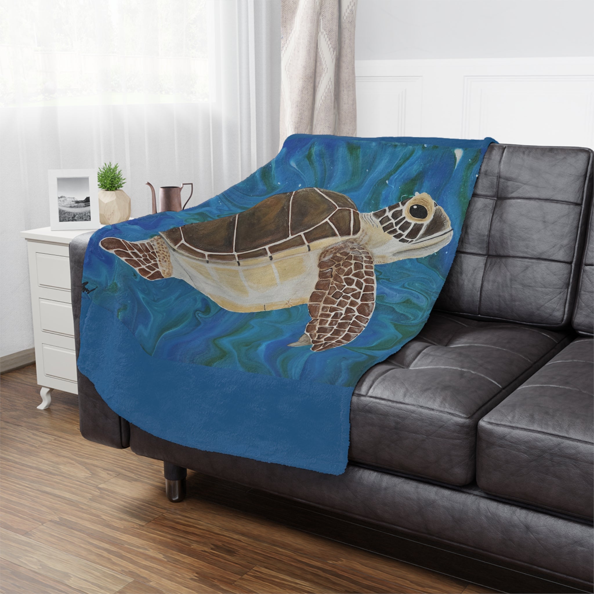 Blanket with a turtle design draped over a gray sofa in a living room.