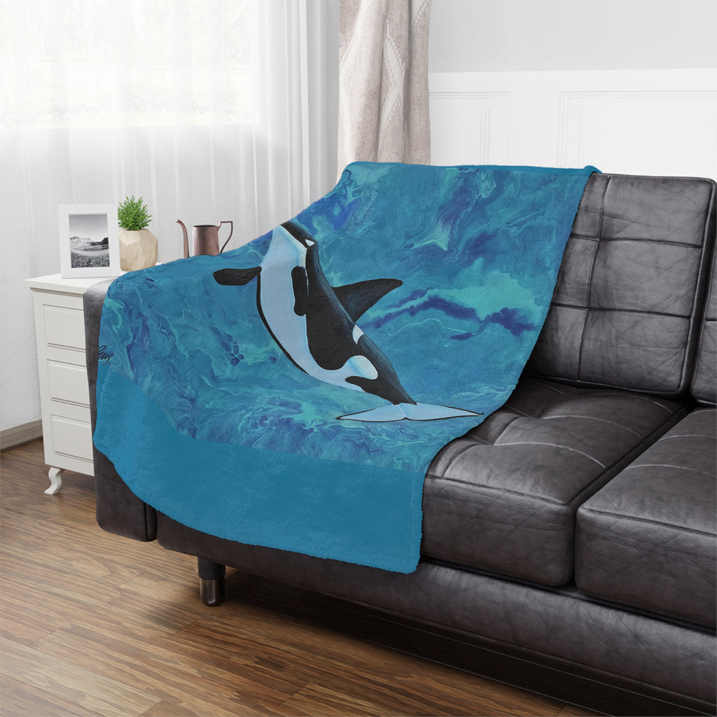 Blue blanket with an orca design draped over a gray sofa in a living room.